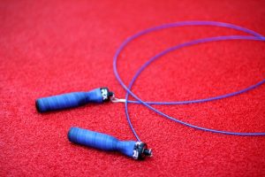 Une corde à sauter bleue posée sur un tapis rouge